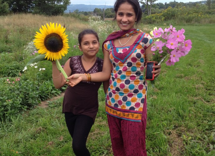 Old Path Farm, a nearby organic farm in Sauquoit, NY, has welcomed refugees to participate in planting, harvesting, cider-making, and other activities throughout the year. In this photo, Pisanti Adhikari and Sabitra Acharya show off the flower bouquets they picked for their mothers. June, 2012. Photographer: Kathryn Stam.