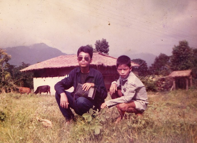 Amber Ranamagar (Left, also from the previous photo) is pictured here with his brother Harka in front of their home in Gelephu, Southern Bhutan, where they lived with their family until they were evicted from their land and their citizenship was revoked by the Bhutanese government in 1992. According to many Bhutanese-Nepali refugees who remember their lives before the conflict, southern Bhutan was a pleasant place with natural beauty and where they appreciated their good health, education, and productive agriculture. Some refugees find it ironic that the Bhutanese government is well known for its “Gross National Happiness,” policy but not for the political conflict and eviction of 100,000, “Lhotshampas,” or ethnic Nepalis living in the South of Bhutan. Photographer: Unavailable. Permission to publish from Mon Ranamagar.