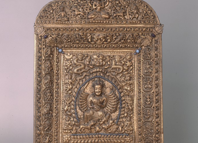 <p>Votive plaque featuring Durga <br />
Nepal <br />
18th century <br />
Courtesy of National Museums Liverpool, 53.87.54<p>
<p>This devotional plaque which features Durga is made from wood, covered with copper gilt and fitted with turquoise and precious stones. The quality suggests it was made for a wealthy Hindu devotee. It is fitted with <em>vajra</em> (Tib. rdo rje, a ritual object that symbolises the properties of the thunderbolt and the diamond – the Sanskrit meaning of <em> vajra</em>) recognised by Hindus, Jains and Buddhists. The inclusion of the <em> vajra</em> makes the cultural and religious exchange of ideas and practice visible. But there is another possible story that the plaque has yet to tell. This one reflects the practice of museum curation and the museum curator’s interest in reconnecting objects to their biographical record and the relationships they once had to people and events. In this case, the unsolved clue comes in the form of a collector’s name noted on the object’s museum label. The collector/owner of the plaque was Sir Charles James Stevenson-Moore (1866-1947) an Indian Civil Service officer. From 1904-07 he was the Inspector General of the Bengali Police force, responsible for the security detail that watched over the ninth Panchen Lama, Thupten Chökyi Nyima (1883-1937) during his visit to Calcutta in 1905-06. Was this high status item then one of the gifts that the Panchen Lama brought to Calcutta for the British Indian government. (Gifts given by dignitaries from across the Himalayan and wider Asian worlds were often stored in specific gift treasuries in Tibet so that they could be given again to unconnected dignitaries at future diplomatic meetings). Had Stevenson-Moore subsequently bought it at auction or from the British India Treasury when the Tibetan gifts were sold off? Had this plaque criss-crossed the Himalaya during its devotional life? This is just one of many hundreds of object biographies still to be uncovered. </p>