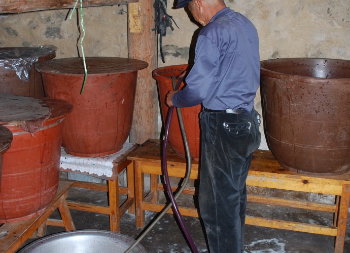 <b><p>Pumping the fermented wine from the barrel containing sediments of grape seeds and skin.</b></p>
In order to filter the wine it is siphoned out into small basins or barrels from the larger buckets using a plastic tube. Any leftover grape skins and seeds sieved out are also saved and stored in a bucket for later grape liquor distillation. The filtered wine is then poured back into the buckets and sealed tightly with plastic film again to ferment.