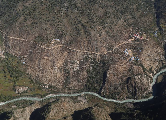 Yangar and Yalbang (Yulwang), September 2017.
The construction of roads gives birth to new settlements and can isolate old ones. The cluster of houses on the left middle corner is Yangar. On the right, the rows of long blue houses constitute the Yalbang school, and above it, the square complex in red is a residential monastery. Houses in blue scattered on the right just below the road are new settlements in Yalbang built following the planning of the road. Like Yangar, old Yalbang village is located further down from the new road, and is becoming deserted. Once a prominent village, Yangar now faces an existential threat from the construction of the new road that alienates it as inhabitants of the old settlement are slowly relocating nearer to the road. Yalbang, on the other hand, holds a brighter future as it was recently declared the headquarters of Namkha Rural Municipality following the 2017 elections that is part of an ongoing process of federal restructuring happening throughout Nepal.