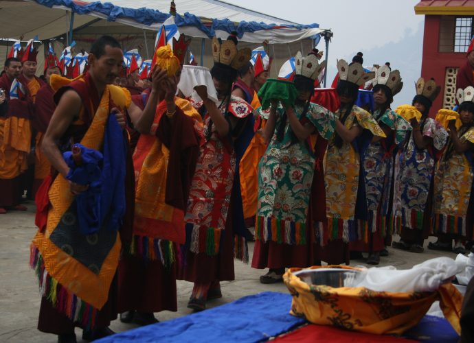 On the fifth day of the fifteen days-long-ritual action, the Eight Goddesses carry the mendrup medicine vessels out of the mandala and the assembly hall to perform the grinding of the medicine. The procession is led by an honorable monk carrying the precious container of the papta (phabs gta’) or ‘fermenting agent,’ which is wrapped in yellow cloth. He is then succeeded by a monk carrying the white vessel of the Centre, followed by the vessels of the East, North, West, and South, according to the Bonpo anticlockwise order. Then come the vessels of the intermediate cardinal directions (Northeast, Northwest, Southwest, and Southeast). Since all of them are in yellow color, their sequence is not distinguishable. The large metal container visible in the front is ready for grinding.