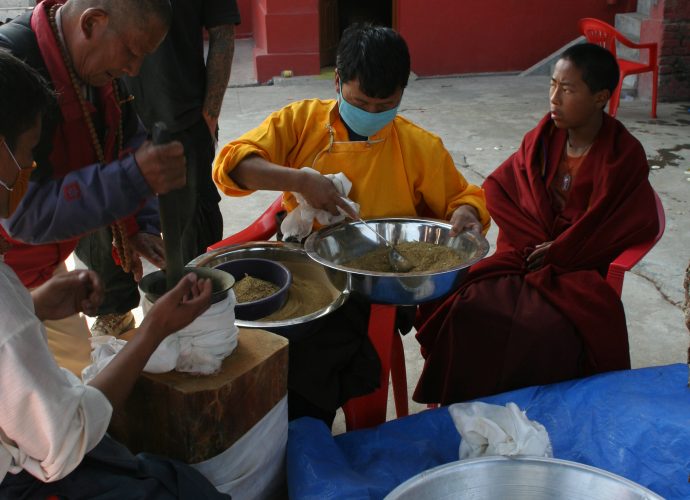 The ritual grinding of the mendrup medicine continues until late afternoon. Amchi Nyima (second from right) and Namsé (far left, in white shirt) direct the mendrup participants in beating the mendrup medicine in the mortar. A visiting practitioner from Himalayan Bonpo communities is just taking part at the pestle (second from left), being watched by a Western Bonpo follower who has already had his turn (third from left). Amchi Nyima pours the raw ingredients into the mortar with a ladle. He then sieves the ground mixture so that only fine powder constitutes the final empowered mendrup medicine. A young monk (first from right) keeps them company during the grinding. Once the grinding is completed, the mendrup medicine is returned to the mandala of the ritual in the center of the assembly hall.