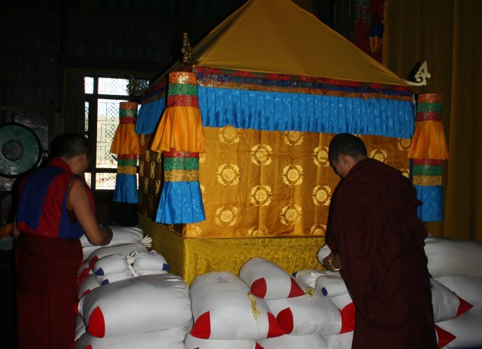 All the mendrup medicine bags are then arranged around and below the special ritual structure containing the mendrup mandala. The structure is of yellow color. Here, the blue color of the cardinal direction of the South is visible, as well as some of the red color of the West. Monks are organizing the small and large bags of the mendrup medicine around the mandala.