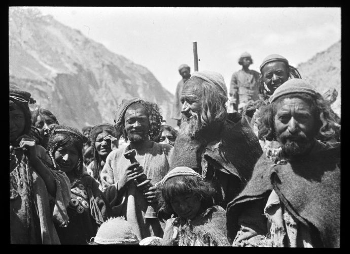 The men are wearing the round homespun caps that are distinctive to Baltistan: men’s caps and clothes were left in the natural colour of the wool, but women’s hats and dresses were normally dyed. The top of the men’s heads is closely shaved whereas they carry long sidelocks over their ears: this hairstyle was commonplace in the first half of the 20th Century, but has since died out.